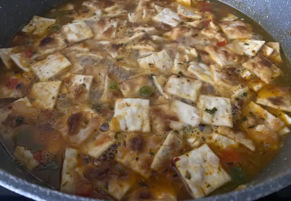 Gazpacho marinero alicantino burbujeante en una sartén, con trozos de pan tostado y verduras.