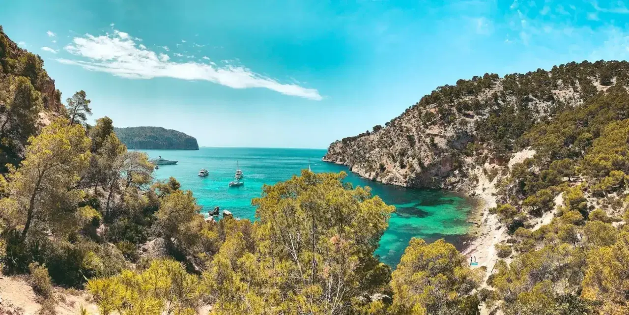 Unas calas de ensueño en la Costa Blanca, con aguas turquesas, vegetación exuberante y barcos navegando.