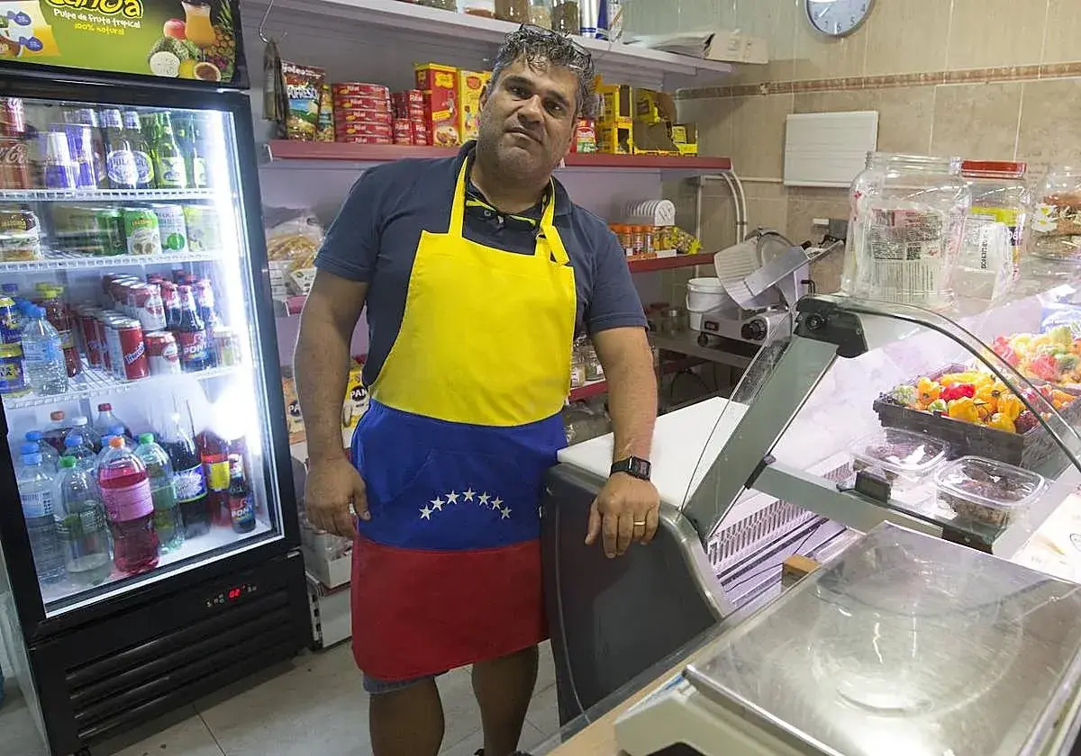 Hombre con delantal de Venezuela en el mercado de Torrefiel, rodeado de productos en neveras y estanterías.