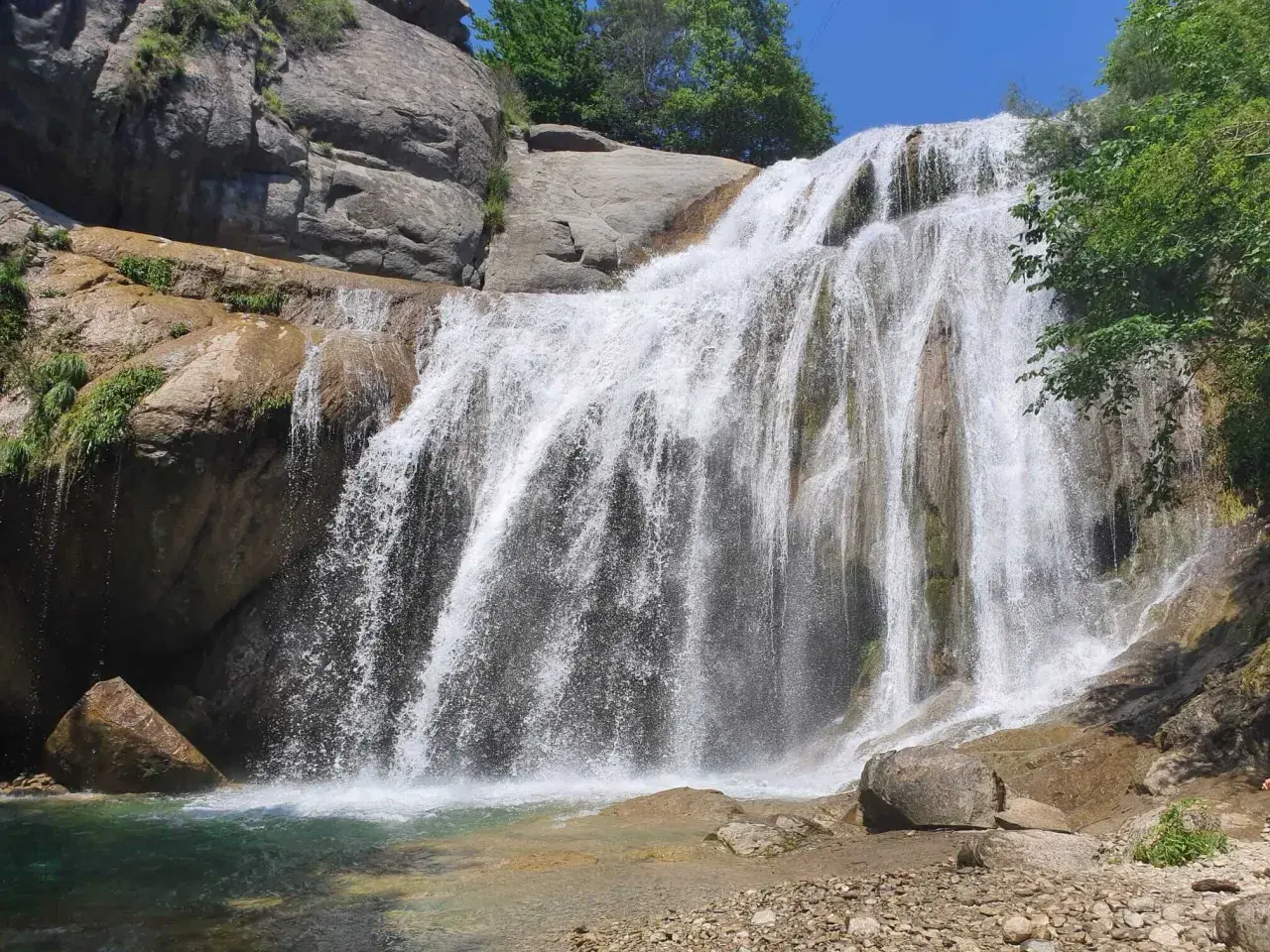 Cascada del Moli, con agua cayendo sobre rocas y vegetación exuberante, formando una piscina natural.