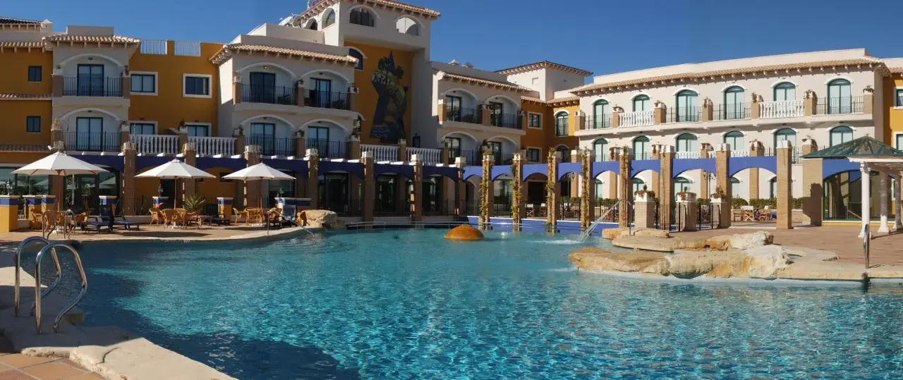 Piscina cristalina frente al hotel La Laguna Spa & Golf, con tumbonas, sombrillas y arquitectura mediterránea.