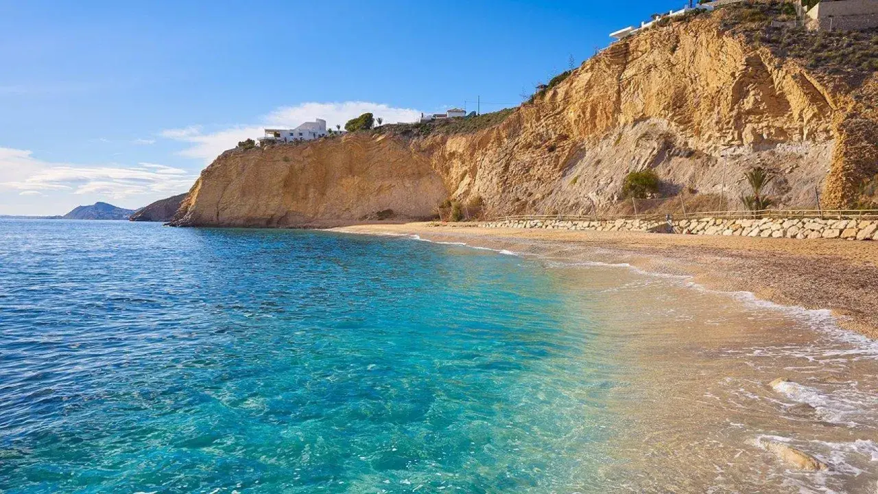 Aguas cristalinas y playas tranquilas en Alicante, con acantilados dorados y casas blancas en la cima.