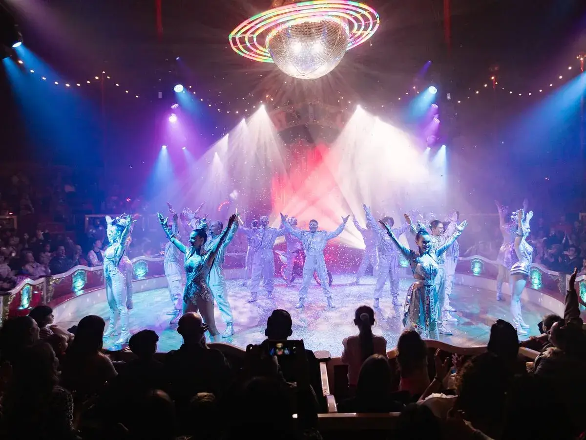 Artistas del circo Raluy en Alicante, bajo una bola de discoteca, con confeti cayendo y público aplaudiendo.