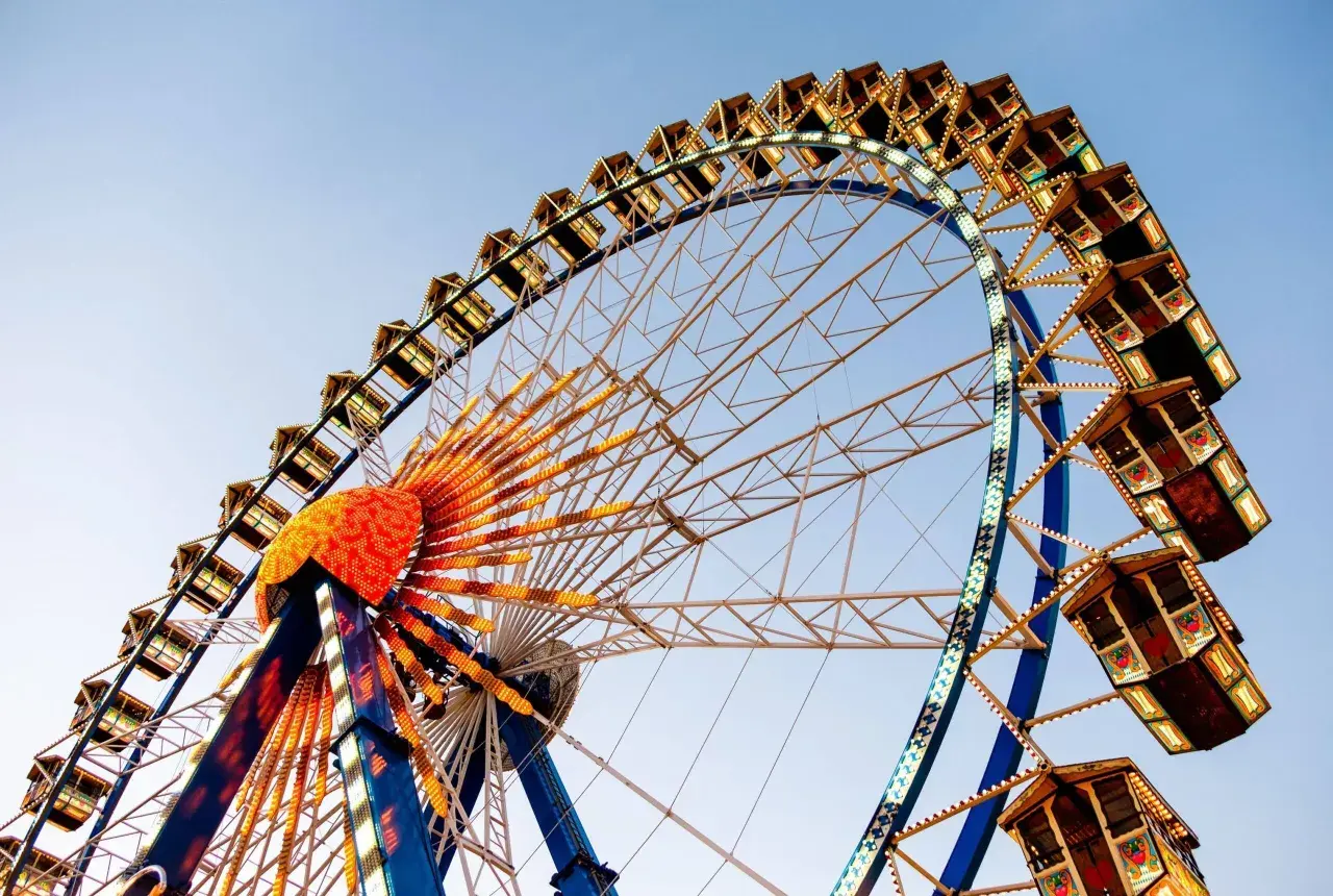La noria iluminada, una de las atracciones principales de la feria de Valencia, se alza contra el cielo azul.