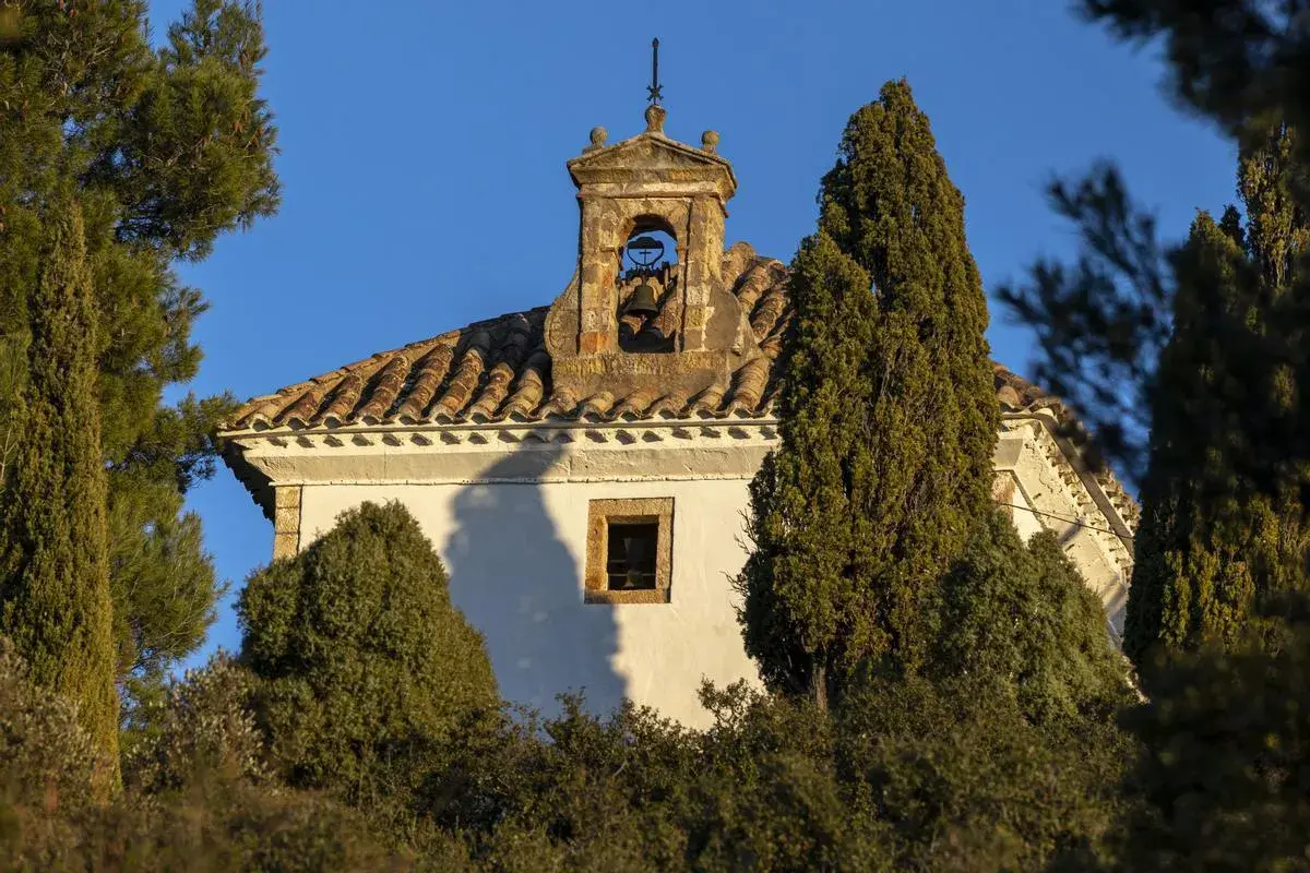 Campanario de piedra con campana, parte del castillo de Villamalefa, rodeado de vegetación y bajo un cielo azul.