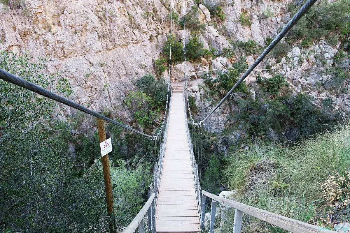 Puentes colgantes de Chulilla, un camino de madera suspendido sobre un barranco rocoso, rodeado de vegetación.
