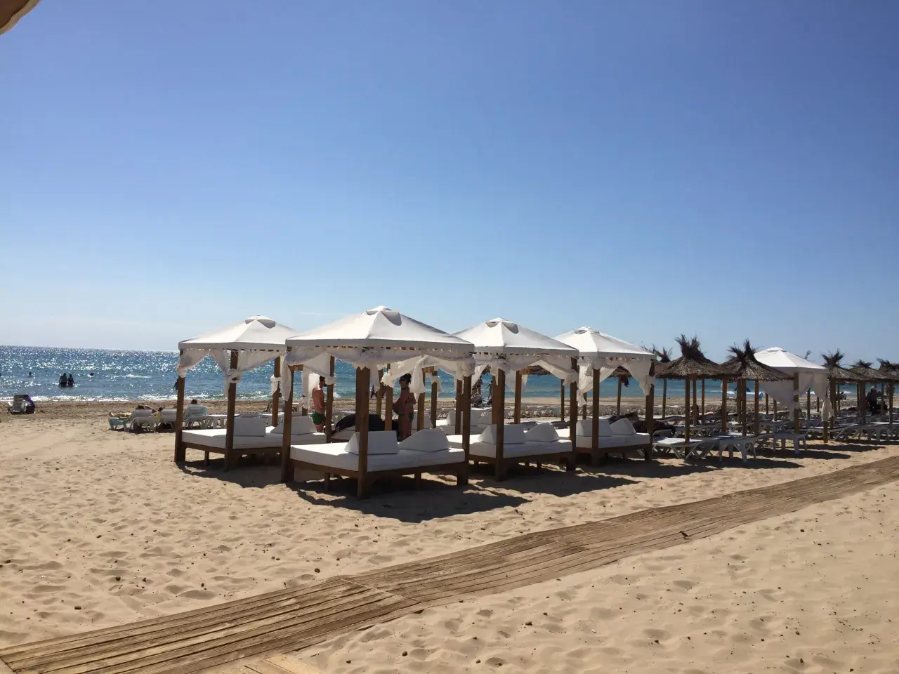Días soleados en la playa Carabassi, con toldos blancos y camas de día listas para el relax junto al mar azul.