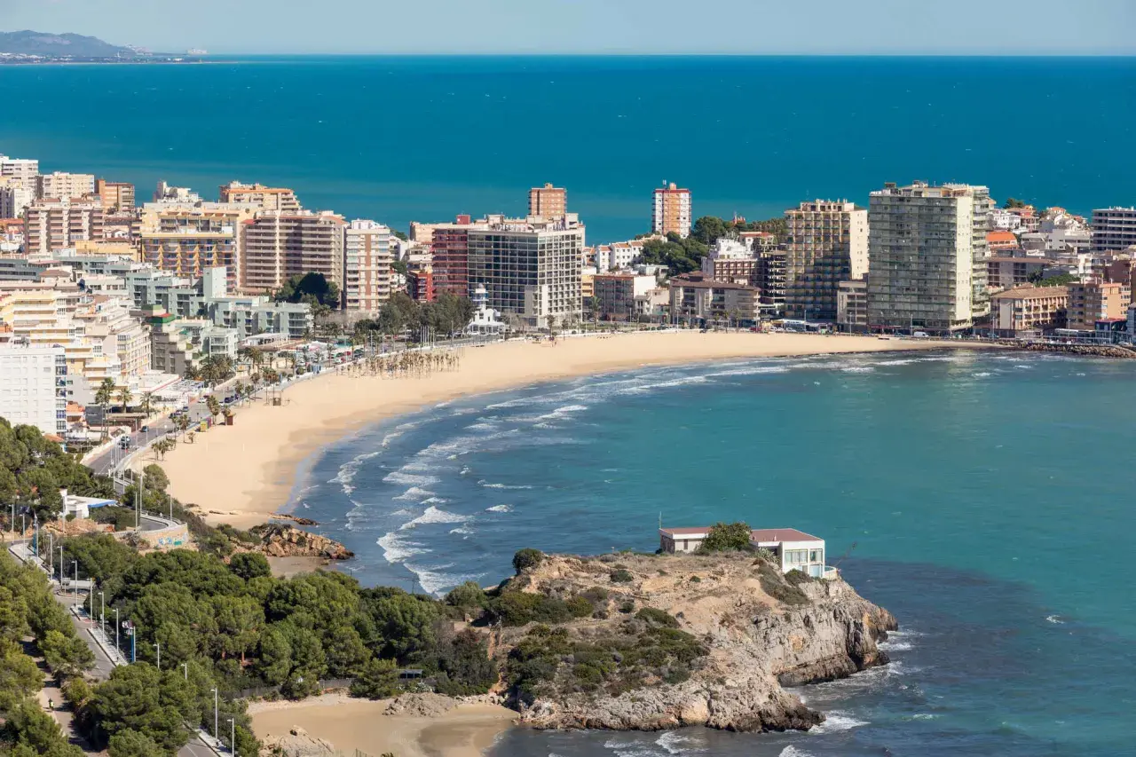 Vista panorámica de la **playa de la Concha Oropesa**, con edificios residenciales, el mar azul y una costa rocosa.