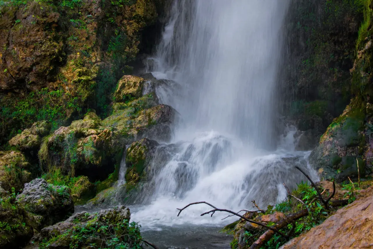 Cascada con rocas cubiertas de musgo y vegetación exuberante.