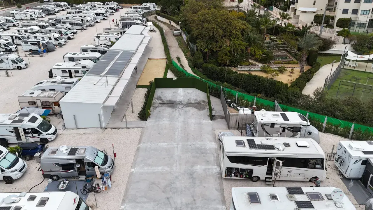 Amplio camper park en Alicante con numerosas autocaravanas y caravanas aparcadas, algunas con paneles solares.