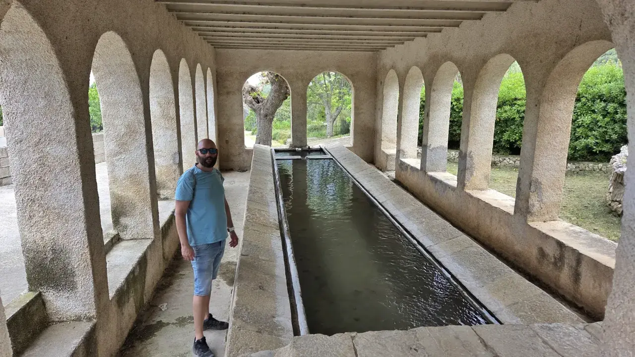 Un hombre posa junto a una larga pila de agua, un lugar que parece la "catedral del senderismo" por su arquitectura y entorno natural.