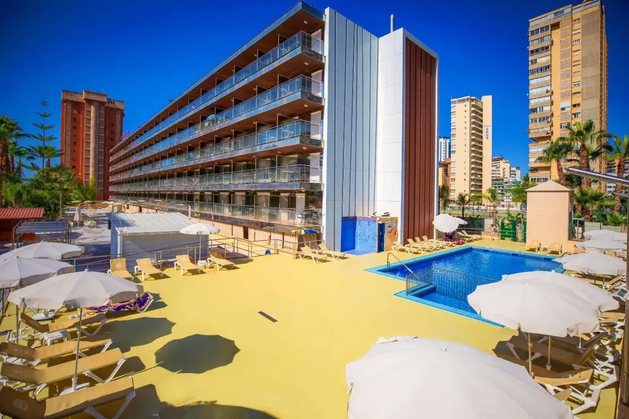 Terraza soleada con piscina y tumbonas en el hotel Diplomatic Benidorm. Edificio moderno con balcones y palmeras.