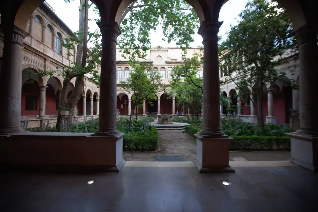 Patio interior con arcos y columnas en el barrio del Carmen, Valencia. Jardín frondoso con fuente central y árboles.