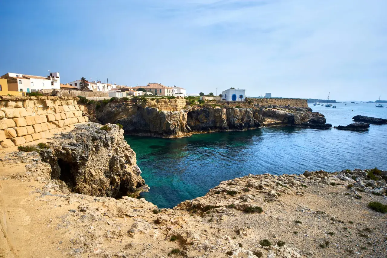Explora la isla de Tabarca: casas blancas sobre acantilados rocosos, aguas cristalinas y barcos en el horizonte. Un lugar para descubrir.