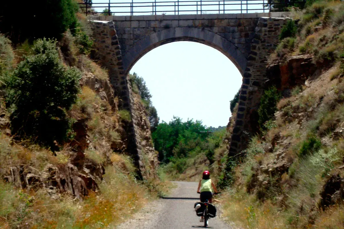 Ciclista pedalea por la vía verde Valencia bajo un antiguo puente de piedra.
