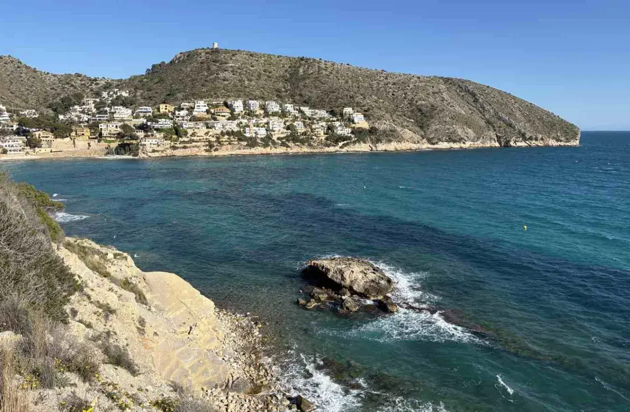 Vista de calas y acantilados con casas blancas en la ladera, aguas turquesas y un peñasco en el mar. Playas bonitas cerca de Benidorm.
