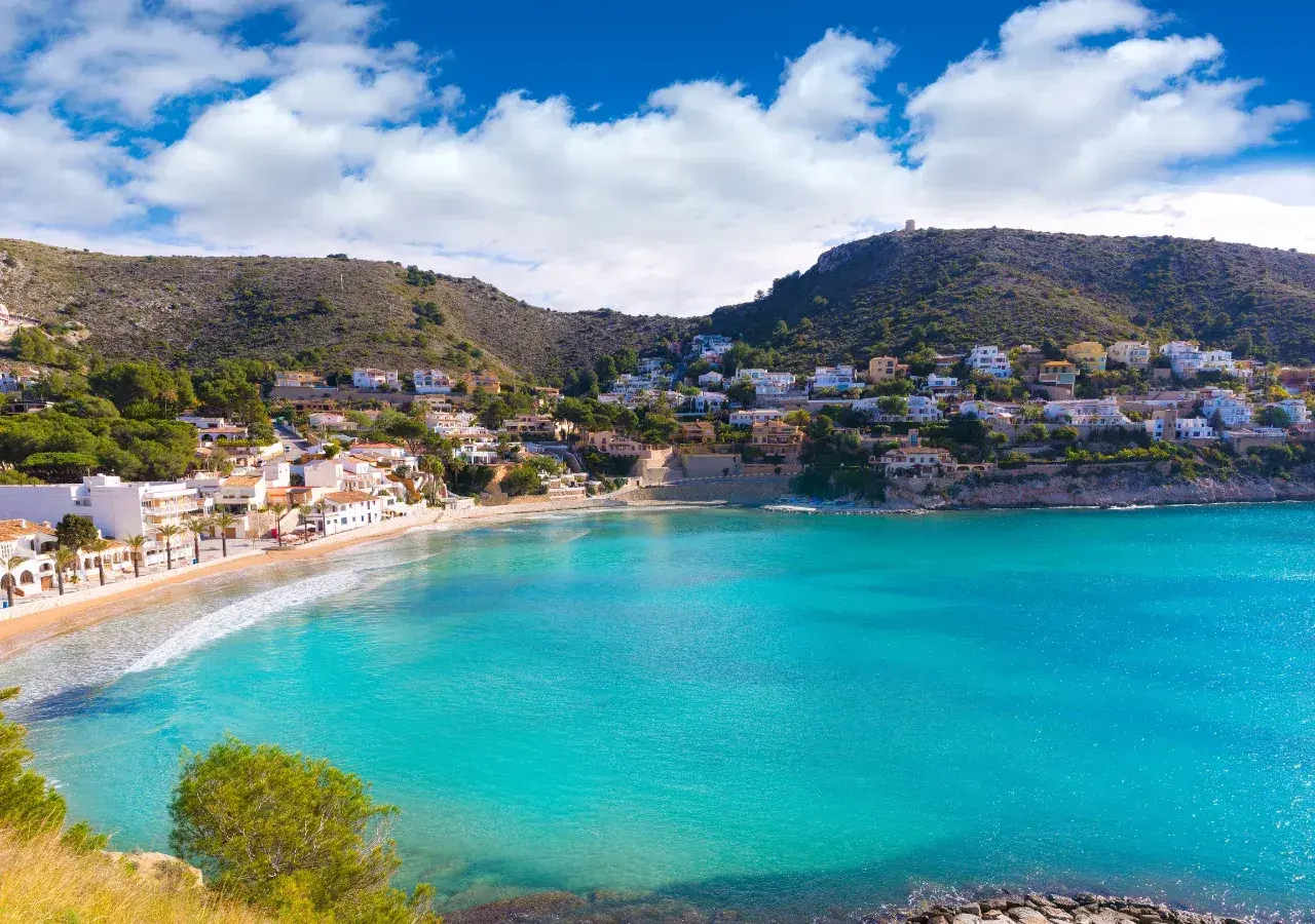 Bahía de aguas turquesas en cala el Portet, con casas blancas y verdes colinas.