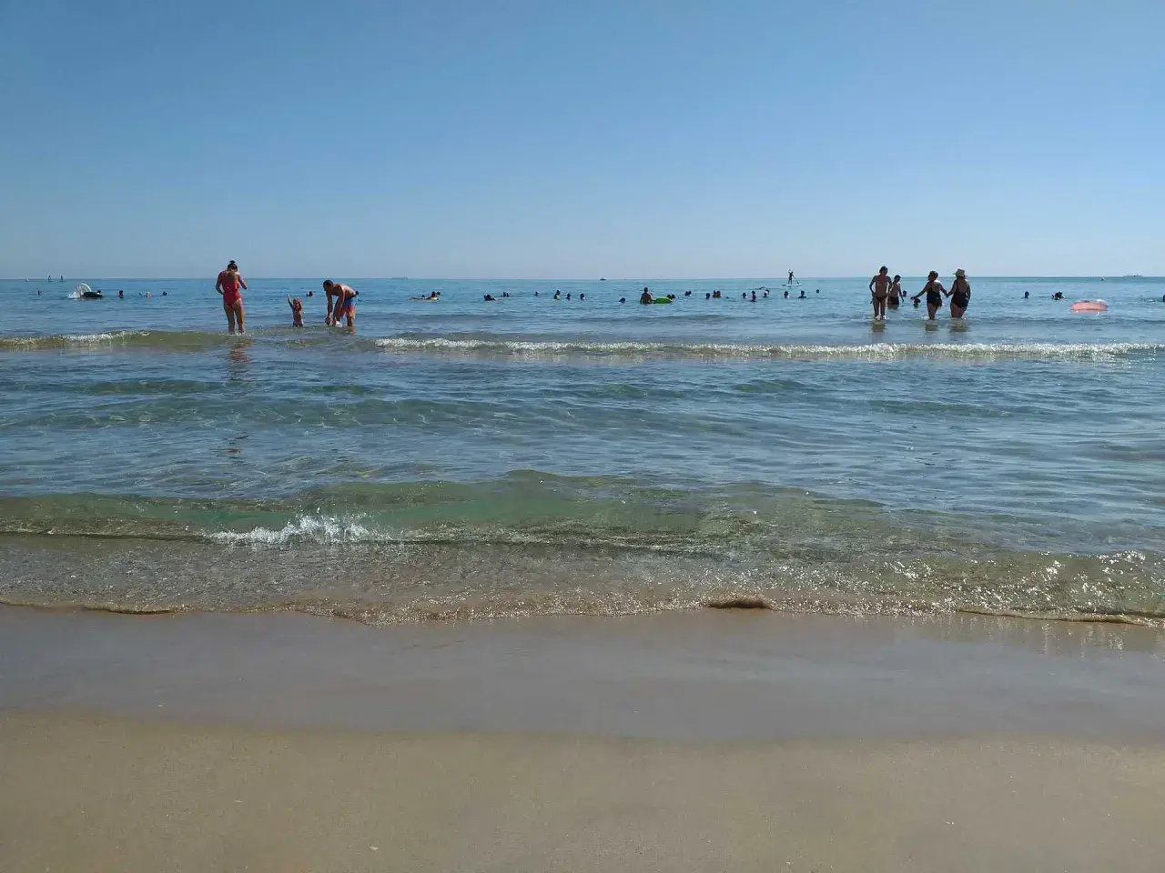 Gente disfrutando del mar y la arena en les palmeretes. El agua cristalina y el cielo azul invitan a un día perfecto.