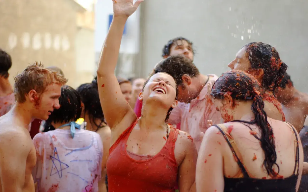 Gente feliz y empapada de tomate en la Tomatina, con una mujer riendo a carcajadas y el brazo en alto.