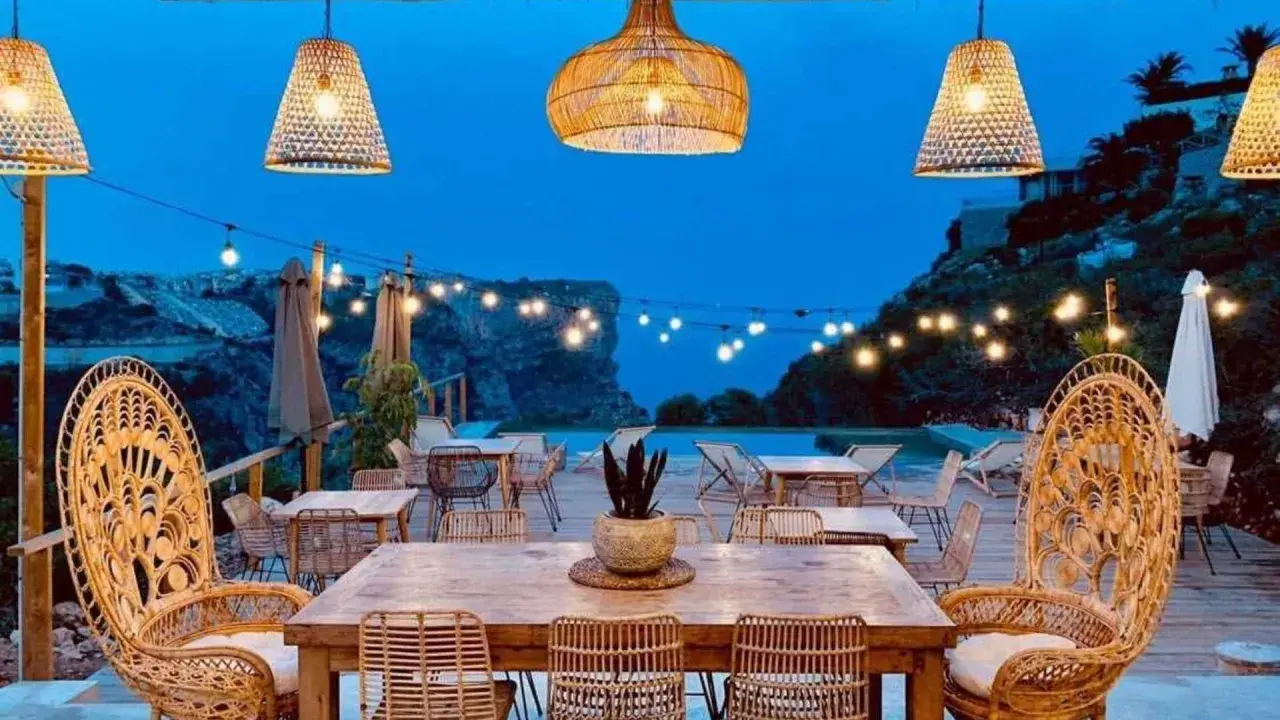 Un rincón de ensueño en el **dreamsea mediterranean camp**. Mesas de madera, sillas de ratán y luces cálidas bajo un cielo estrellado.