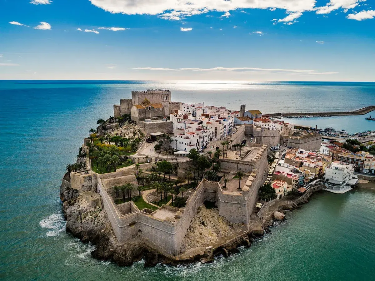 Castillo de Peñíscola sobre el mar, con sus murallas y casas blancas. La peñíscola playa se extiende a su lado, invitando a disfrutar del sol y el Mediterráneo.