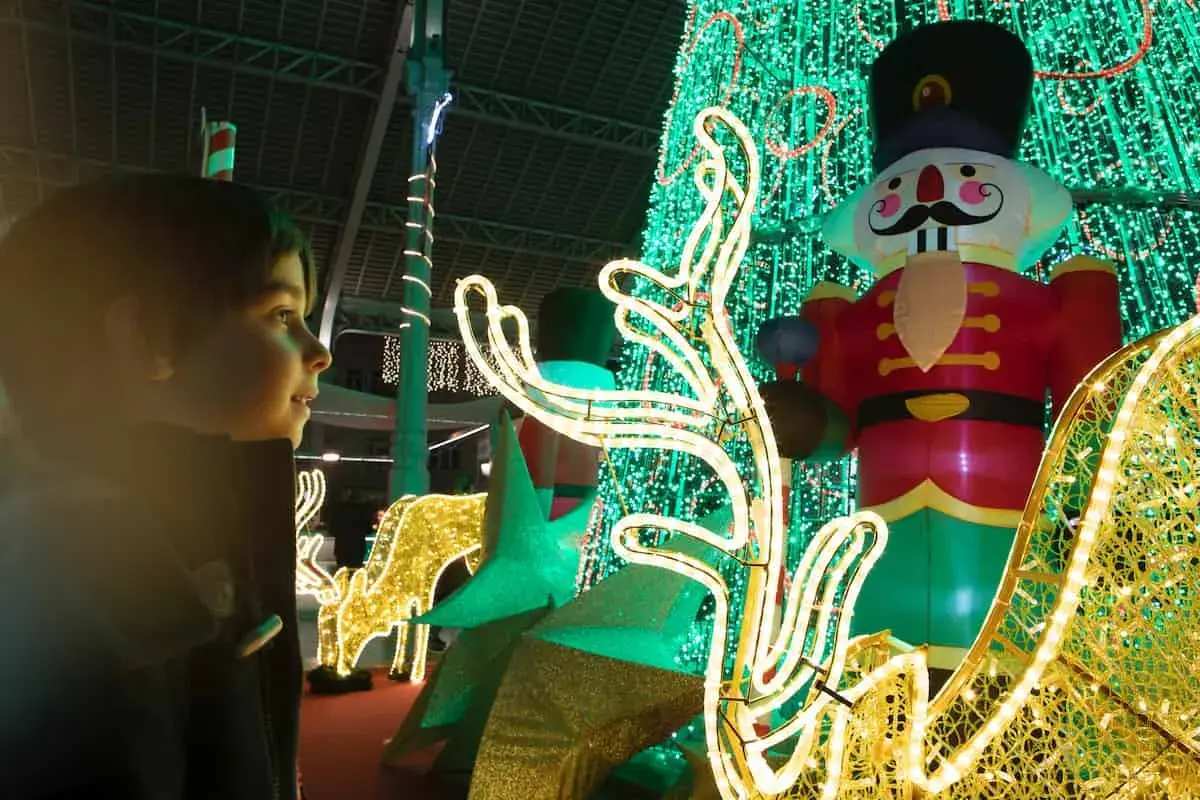 Niño mira con asombro el encendido de luces de Navidad en Valencia, con un cascanueces gigante y renos luminosos.