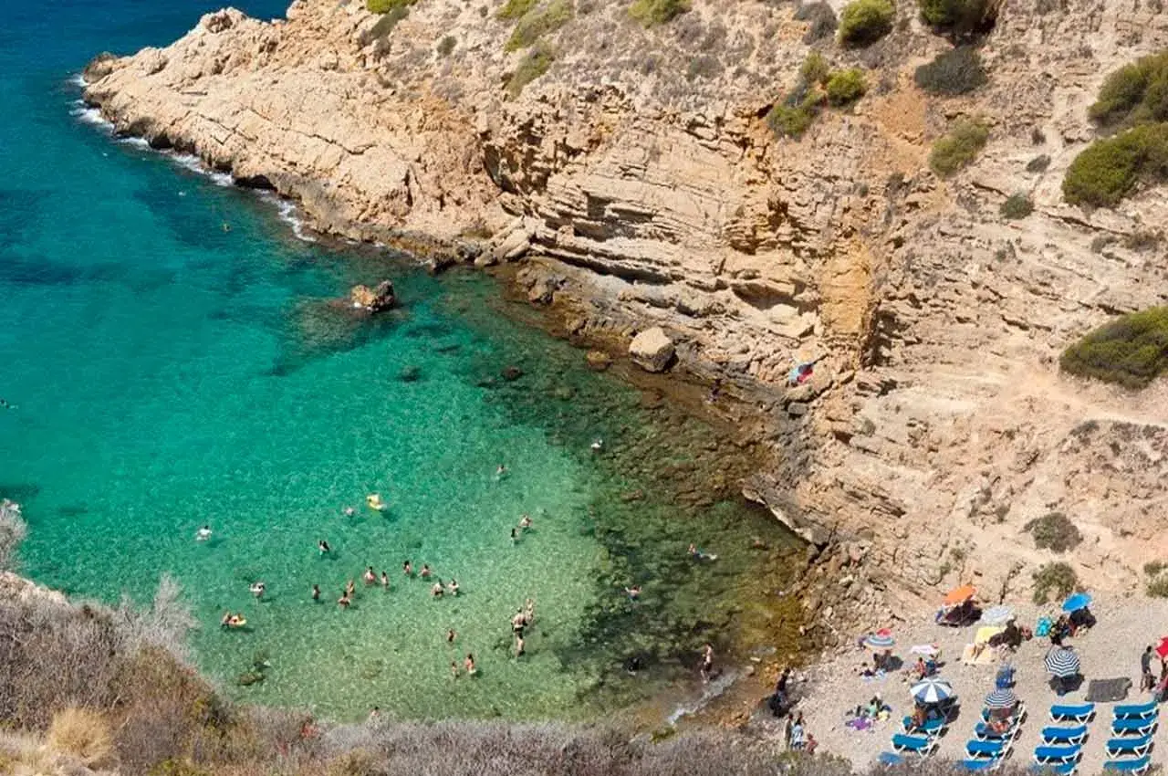 Aguas cristalinas y gente disfrutando en una cala rocosa, un paraíso que recuerda a las mejores calas de Benidorm.
