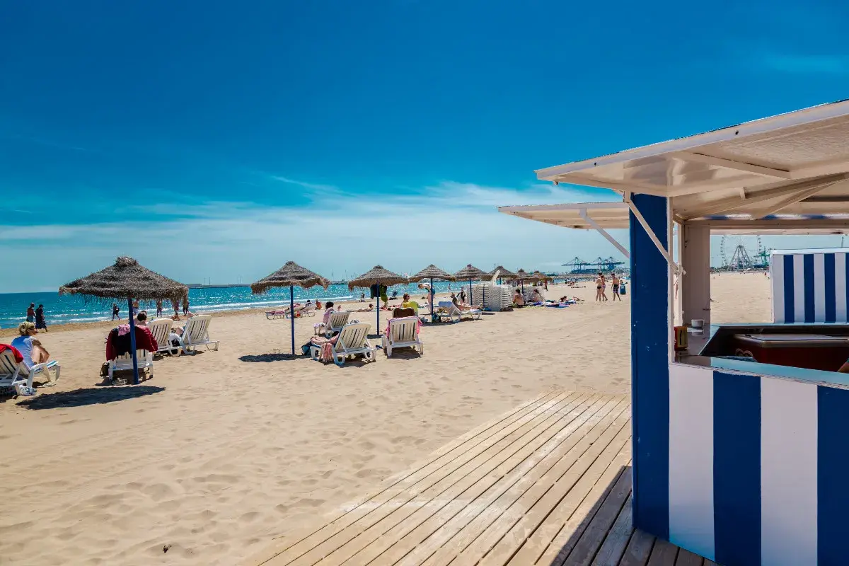 Día soleado en la strand Valencia. Sombrillas, tumbonas y gente disfrutando de la arena dorada y el mar azul.