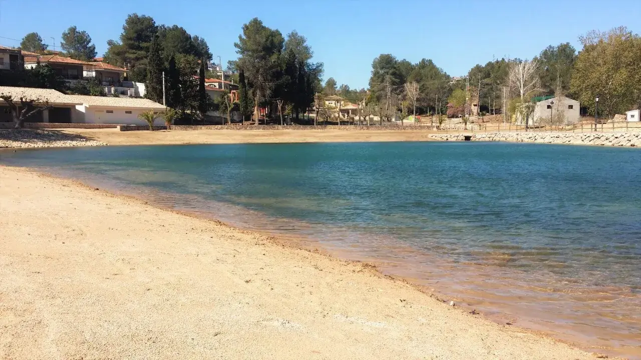 Arena dorada y aguas turquesas en la playa de Monte Navarrés, rodeada de pinos y casas.