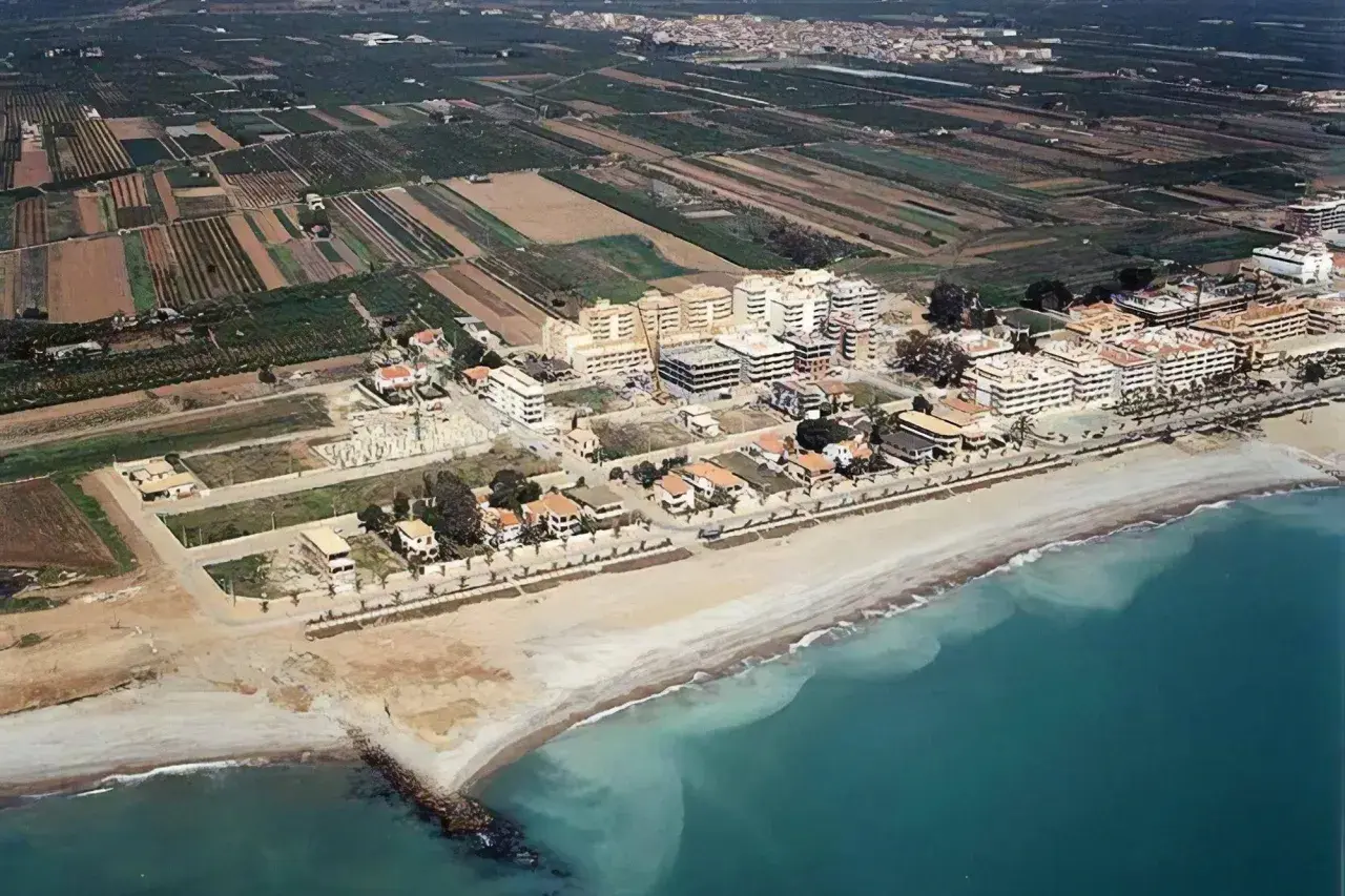 Vista aérea de la costa de Moncofa, con edificios residenciales y campos agrícolas. La playa de Moncofa se extiende hacia el mar turquesa.
