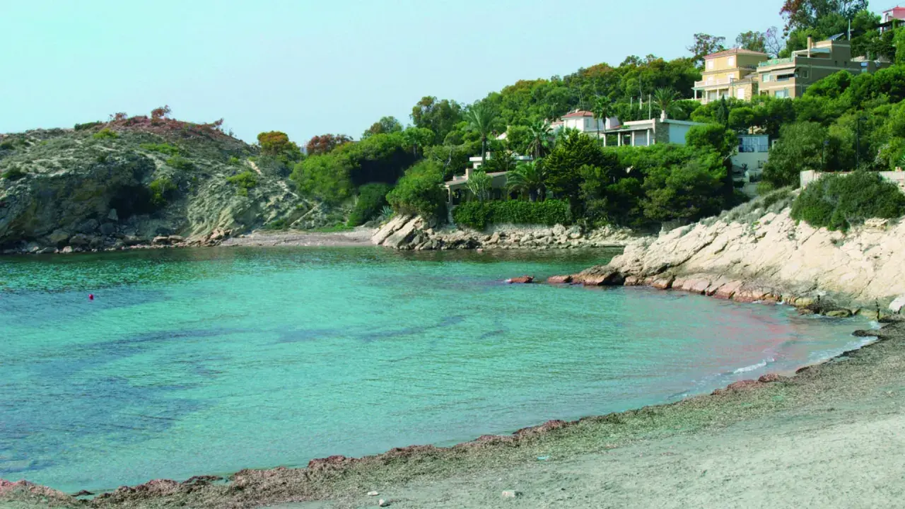 Aguas turquesas bañan la cala d'enmig, con casas blancas y verdes colinas de fondo.