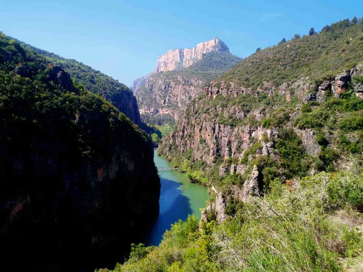 Impresionante desfiladero de Mont-rebei, con un río de aguas turquesas serpenteando entre imponentes paredes rocosas cubiertas de vegetación.