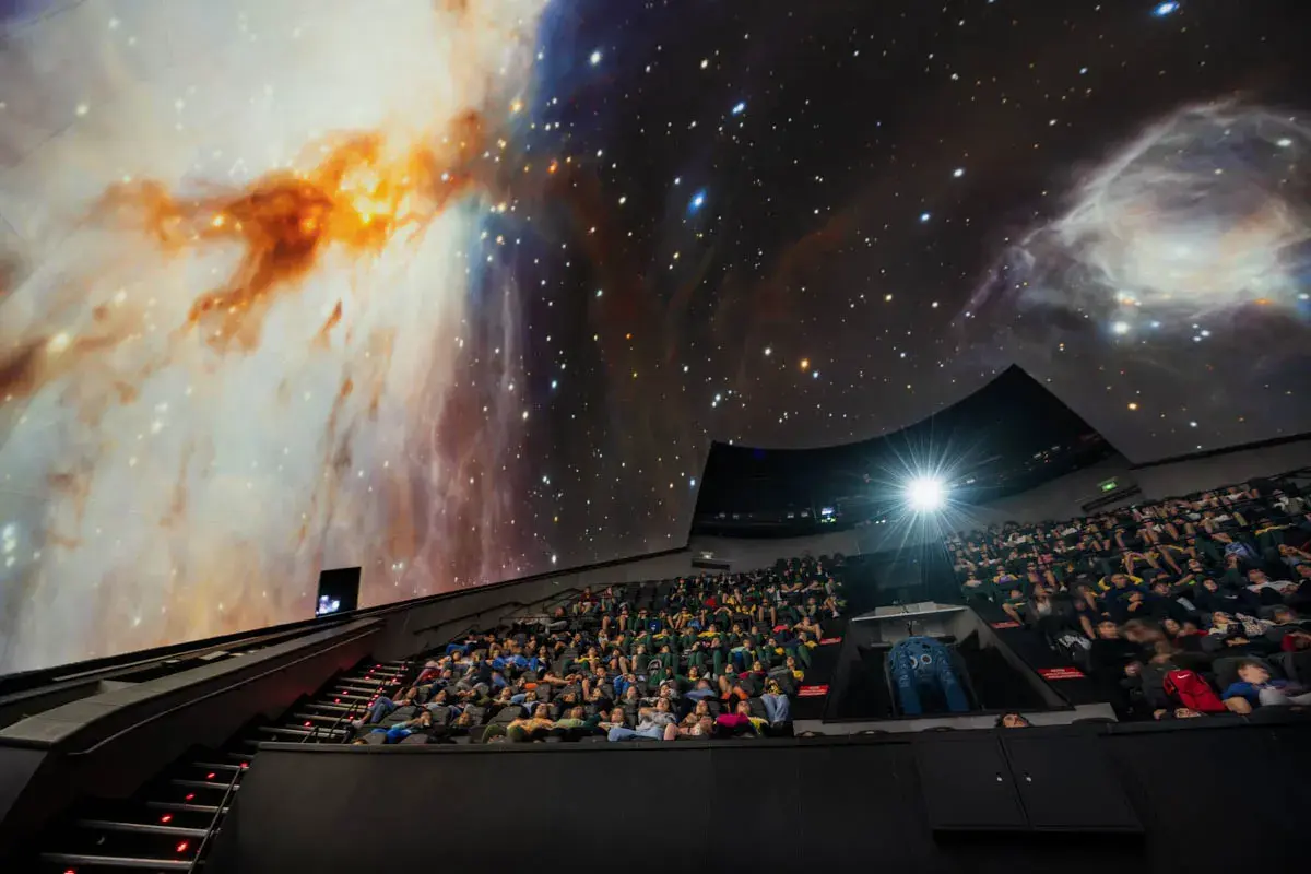 Espectadores en el planetario Valencia, inmersos en una proyección de nebulosas y estrellas.
