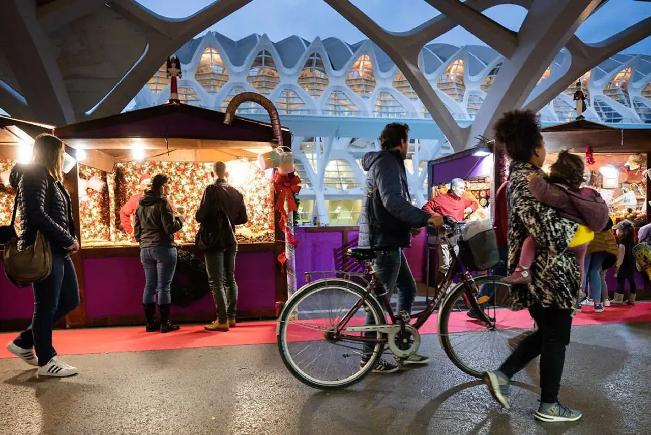 Gente pasea por puestos del **Valencia Christmas Market** bajo una estructura futurista.