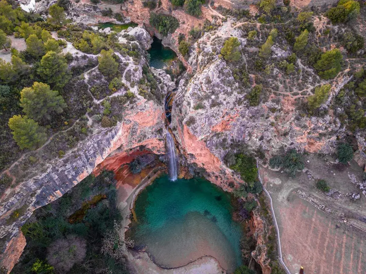 Cascada cayendo en una poza turquesa, rodeada de rocas rojizas y vegetación. Un rincón secreto, como la cueva turche, esperando ser descubierto.