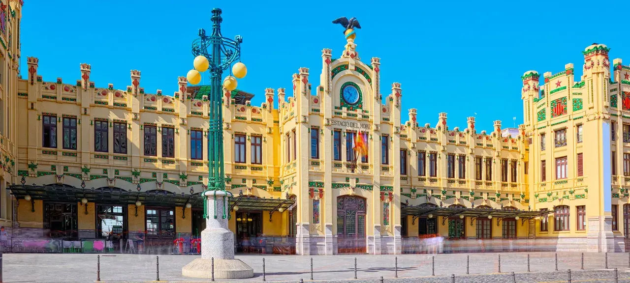 Estació del Nord Valencia, edificio modernista amarillo con detalles verdes y rojos, reloj y águila en la fachada.
