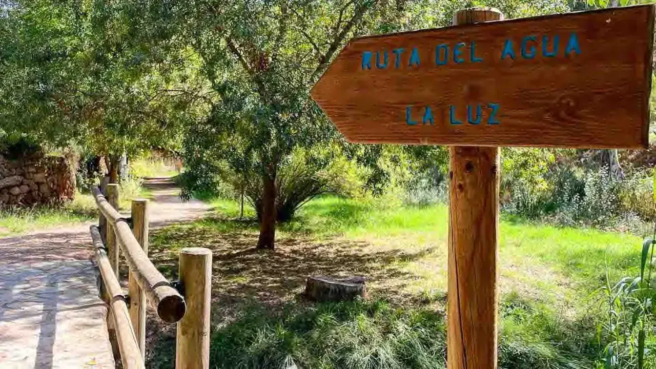 Cartel de madera indica "Ruta del Agua" y "La Luz" en Chelva. Camino de tierra con barandilla de madera.