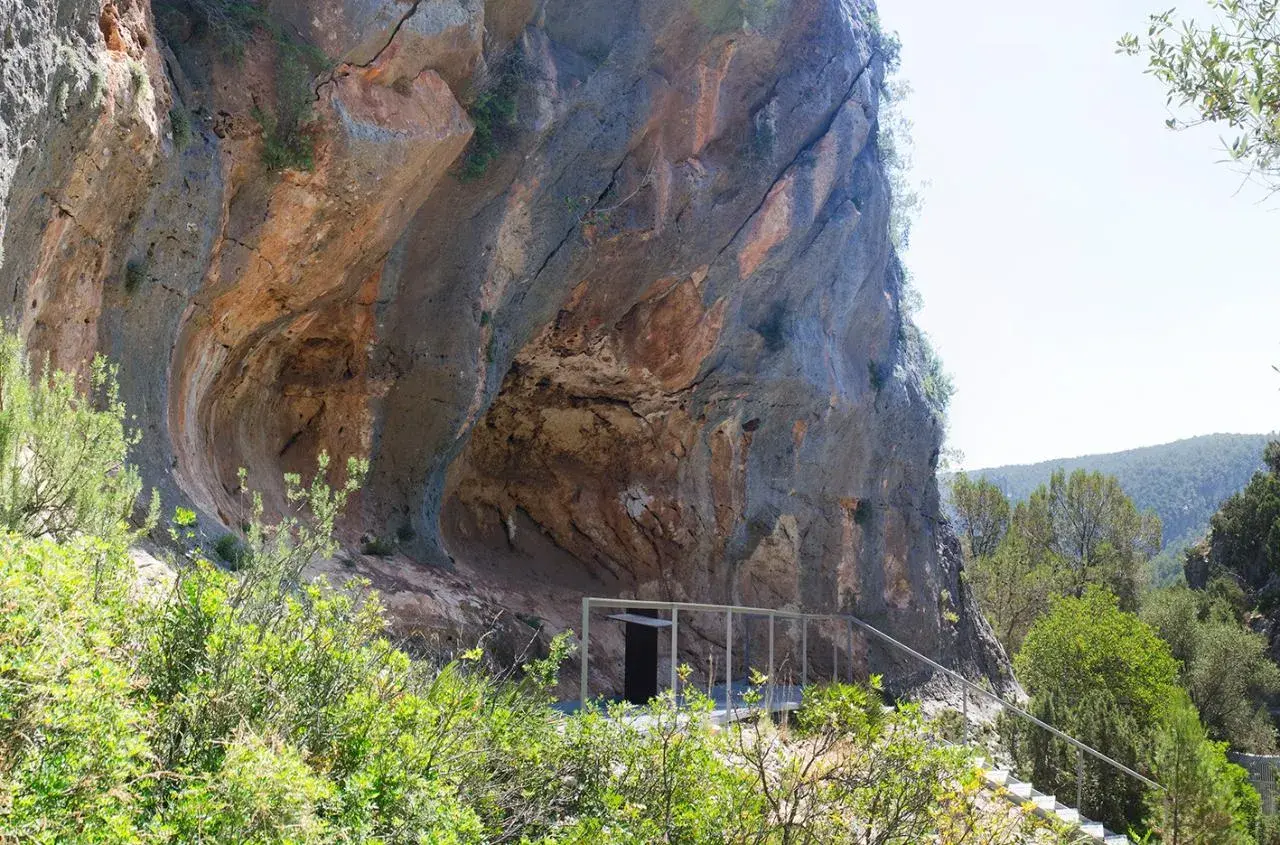 La cueva de la araña, una entrada moderna a una formación rocosa natural, se asoma entre la vegetación.
