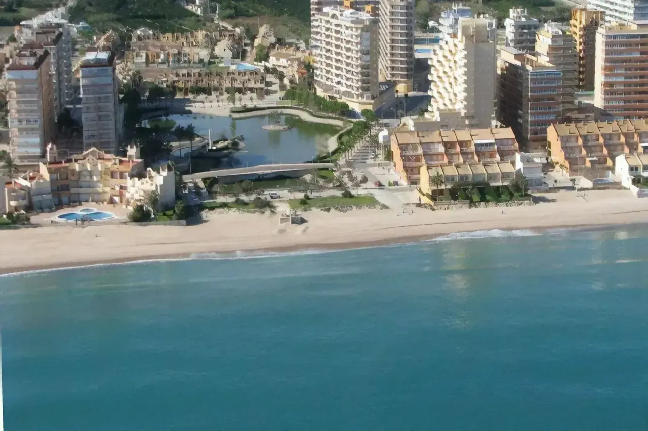 Vista aérea de la playa de la goleta, con edificios residenciales, una laguna artificial y el mar turquesa.