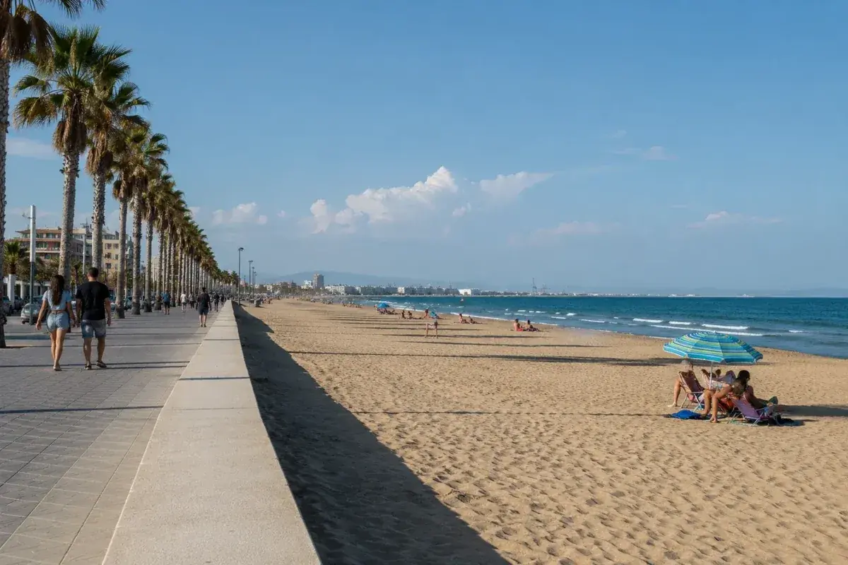 Paseo marítimo con palmeras y gente disfrutando de las **plages valence** bajo un cielo azul.