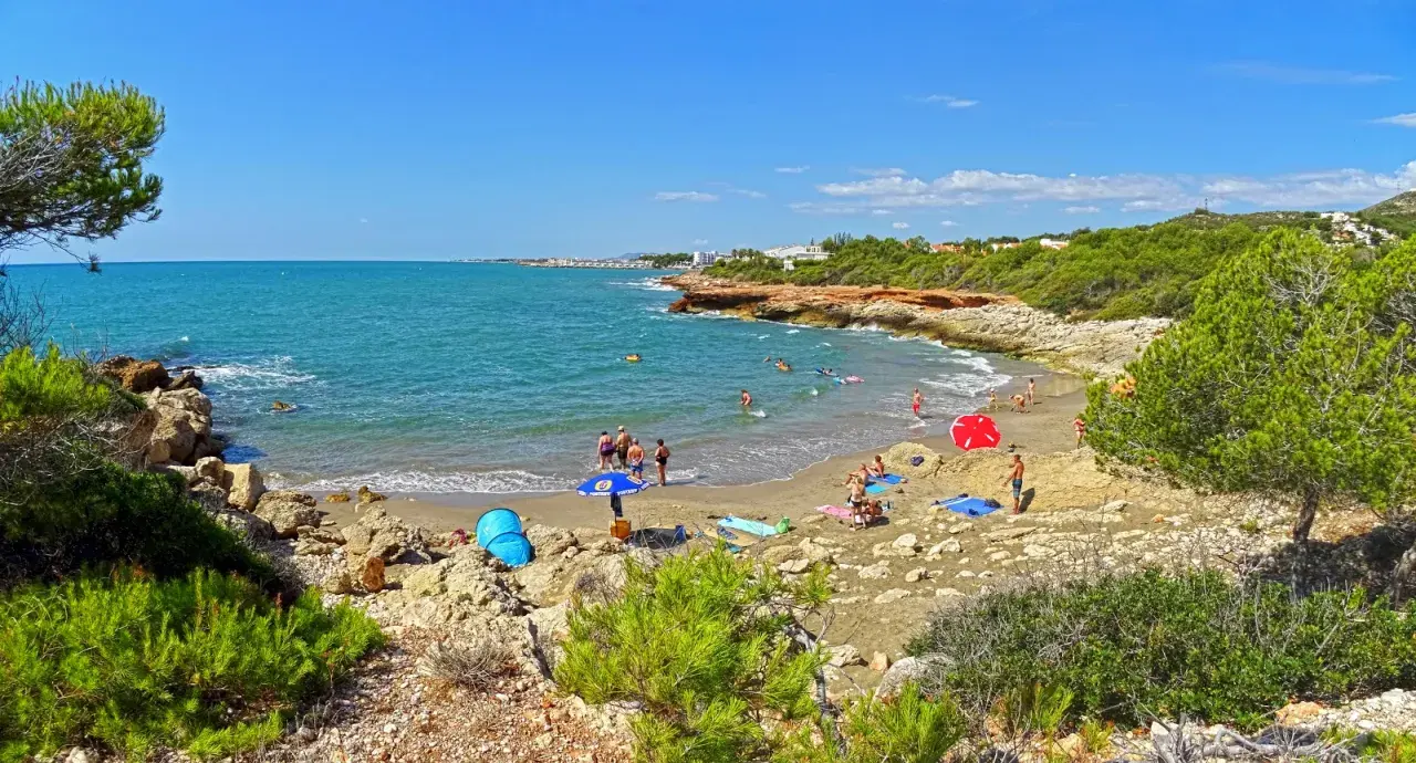 Gente disfrutando del sol y el mar en la cala blanca de Castellón, con aguas turquesas y vegetación mediterránea.