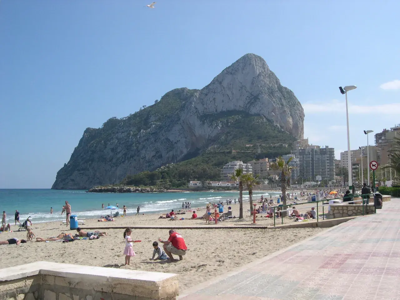 Gente disfrutando del sol y el mar en la playa de la Fossa, con el imponente peñón de Ifach de fondo.