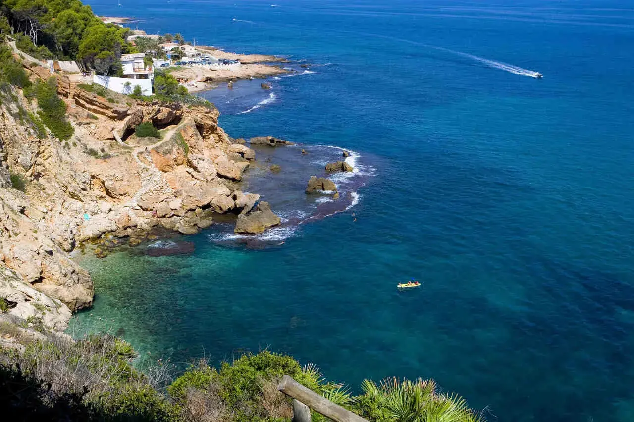 Vista de la cala Les Rotes con aguas cristalinas, acantilados rocosos y un kayak amarillo en el mar azul.