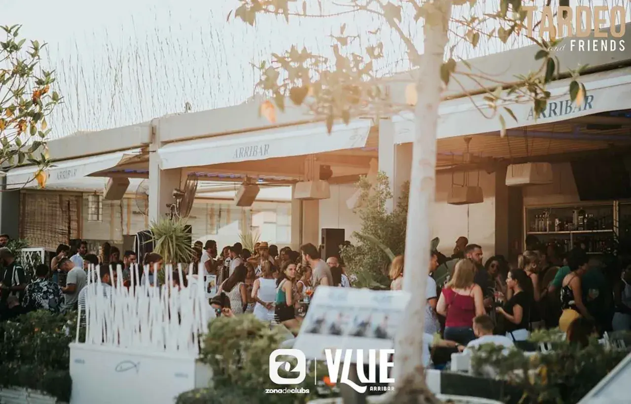 Gente disfrutando en Arribar, un lugar con ambiente de fiesta. El logo de @VLUE destaca.
