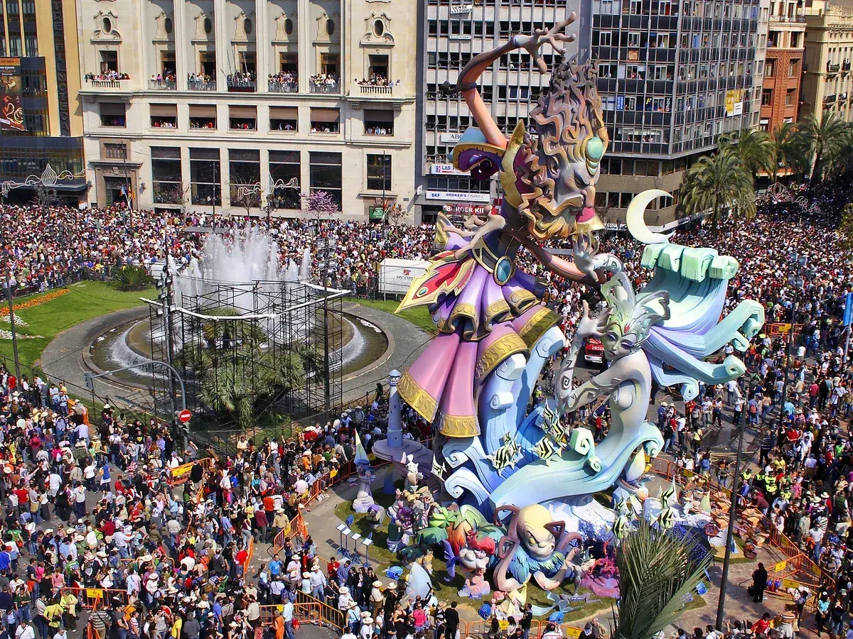 Gigantescas figuras de las mejores Fallas de Valencia, rodeadas de miles de personas, celebran la fiesta en una plaza con fuente.