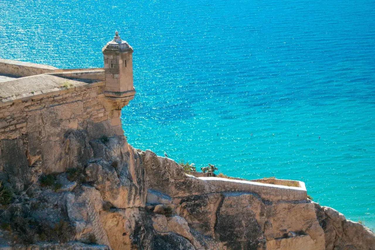 Torreón en el Castillo de Santa Bárbara, con el mar turquesa de fondo. Una vista icónica de la exposición alicantina.