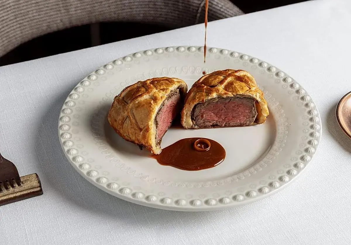 Un Wellington de ternera jugoso, cortado por la mitad, servido con salsa en un plato elegante. Una delicia para probar en los restaurantes de Valencia.