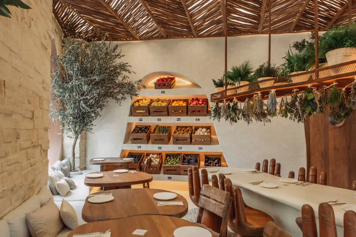 Interior de restaurantes en Valencia con encanto, con estanterías de frutas y verduras frescas, un olivo y mesas de madera.