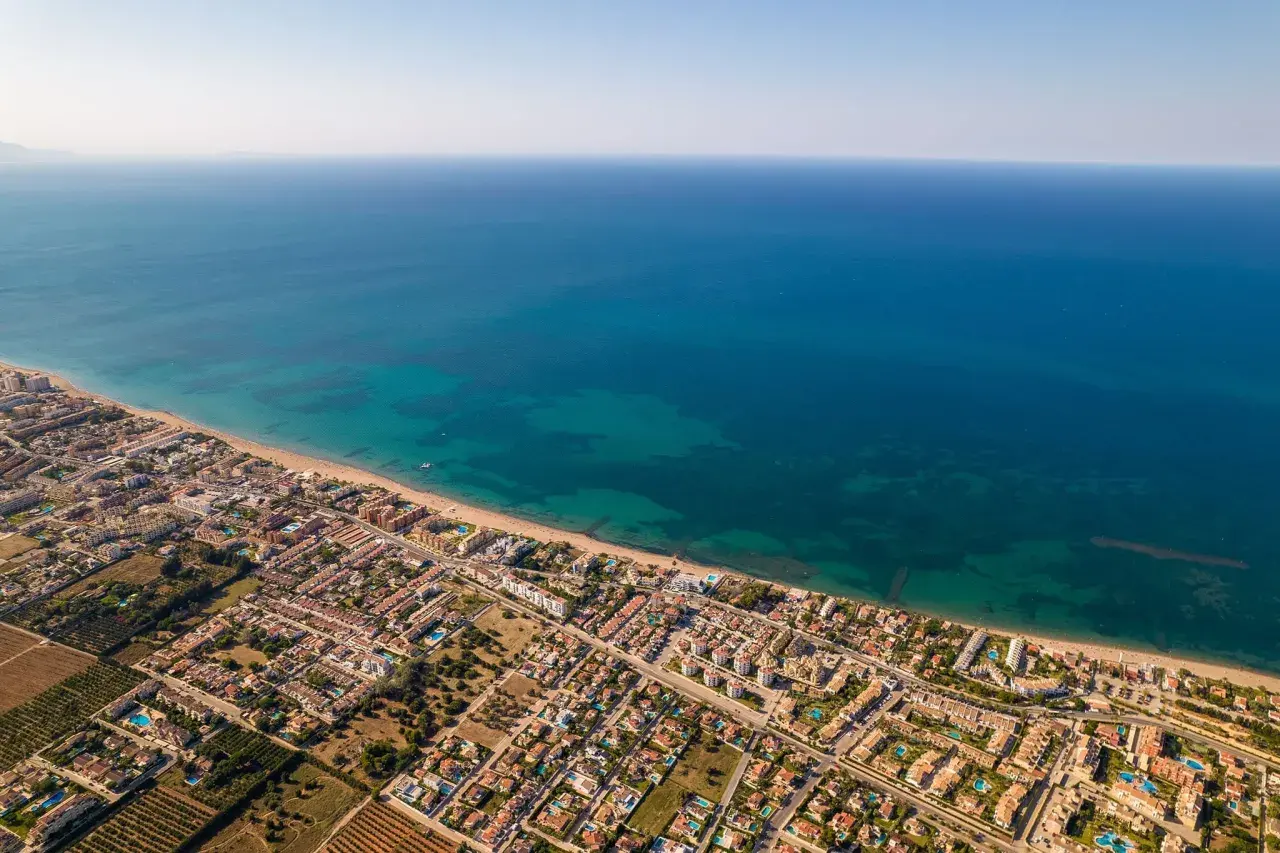 Vista aérea de la playa de arena de Dénia, con el mar azul turquesa y edificios residenciales.