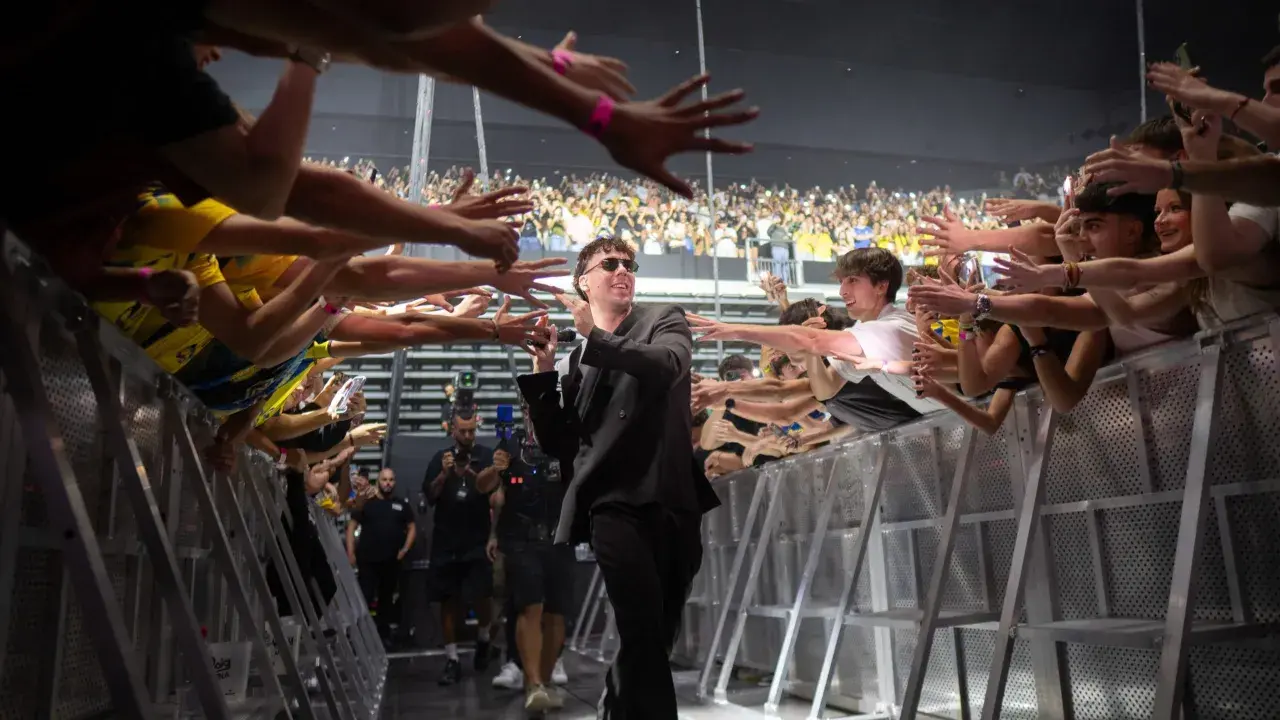 Quevedo saluda a sus fans en un concierto, con manos extendidas y móviles grabando el momento.